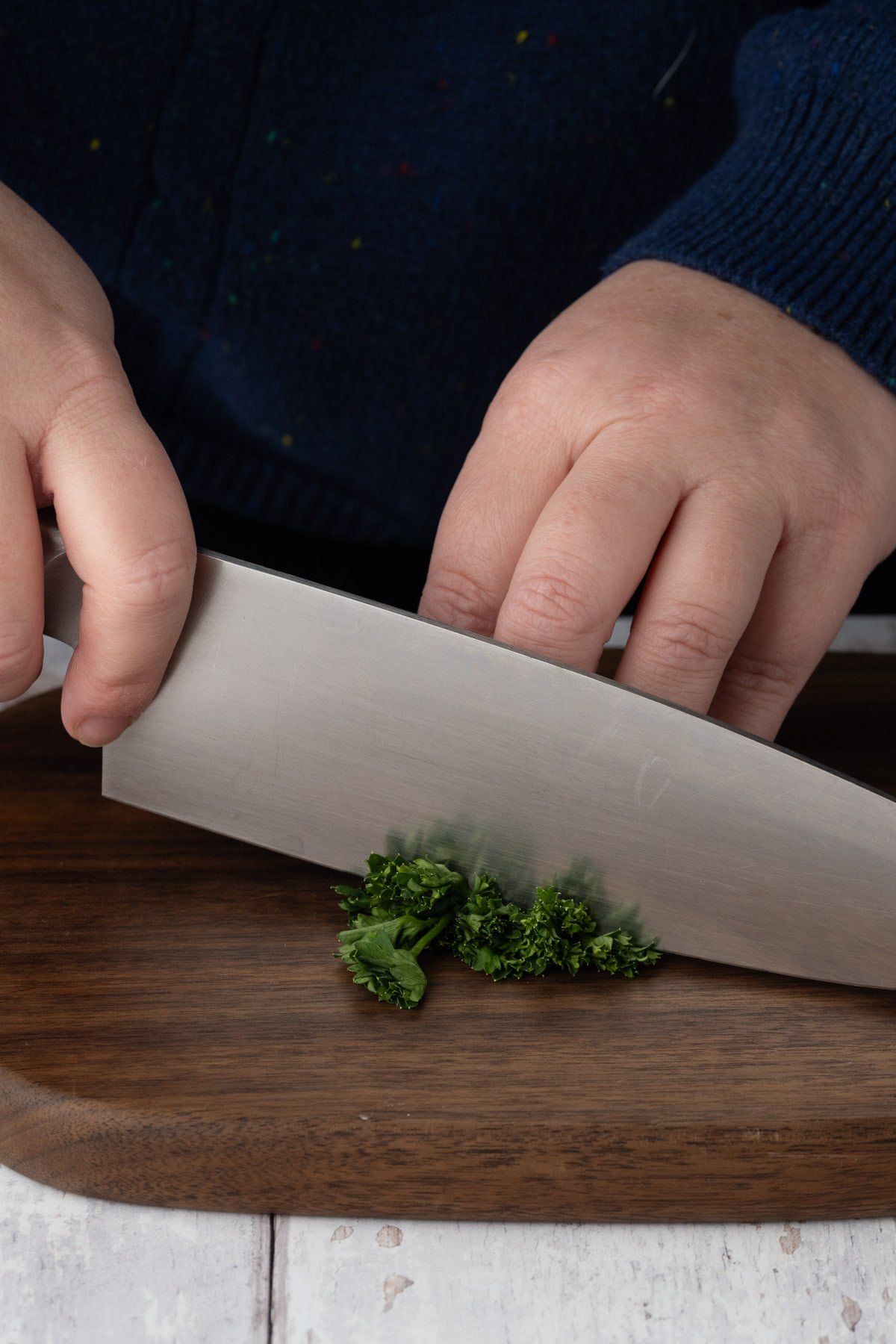 Dicing fresh parsley leaves with a sharp knife on a wooden chopping board. 