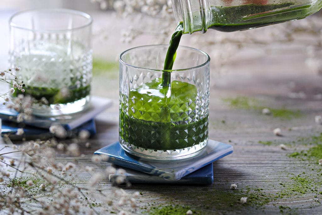 pouring matcha and vodka into cocktail glass with ice