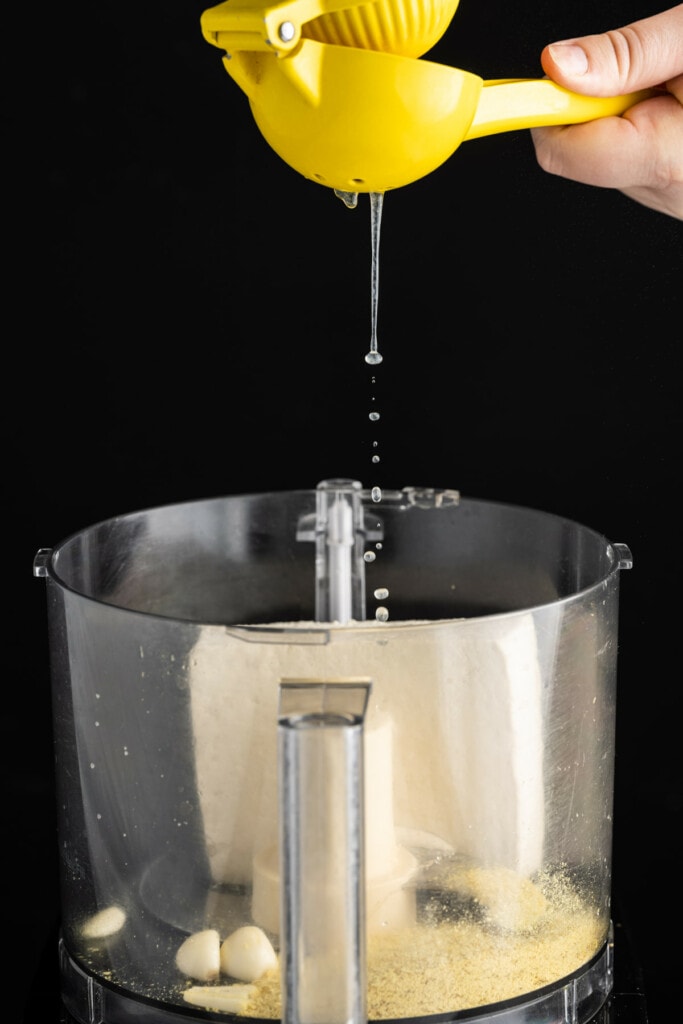 Squeezing fresh lemon juice into food processor for Vegan Spinach Artichoke Dip