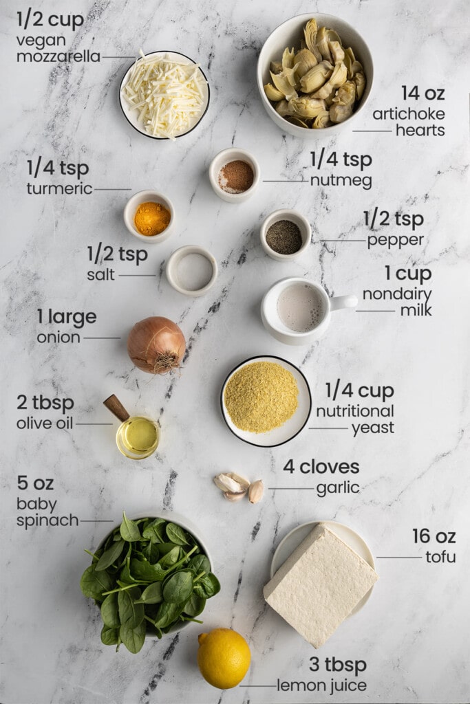 All ingredients for Vegan Spinach Artichoke Dip including tofu, artichoke hearts, onion, garlic, olive oil, spinach, lemon juice, nutritional yeast, non-dairy milk, salt, pepper, nutmeg, turmeric, and vegan cheese
