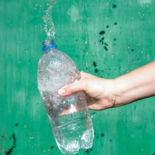 water splashing out of plastic water bottle with green background sideways