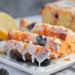 close up of sliced lemon loaf with blackberries and glaze dripping off