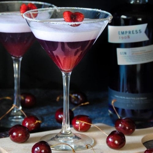two cherry martinis with one on a wooden board
