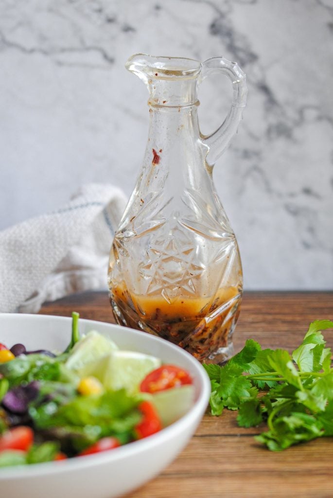 chipotle vinaigrette in a crystal bottle sitting behind a colorful salad