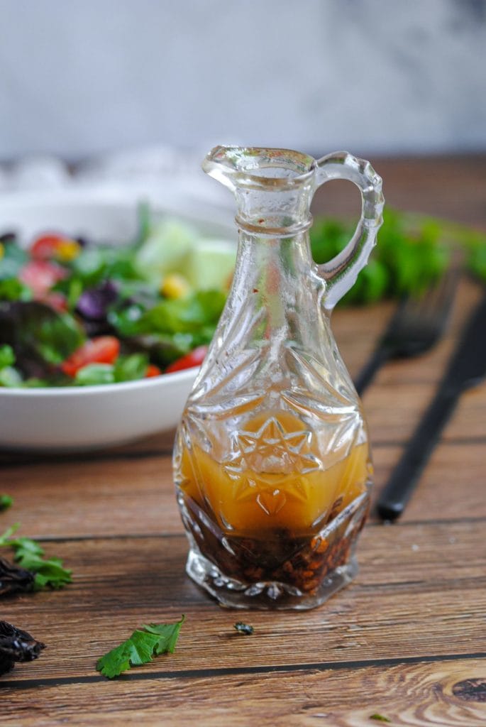 chipotle vinaigrette in a crystal bottle sitting in front of a fresh colorful salad