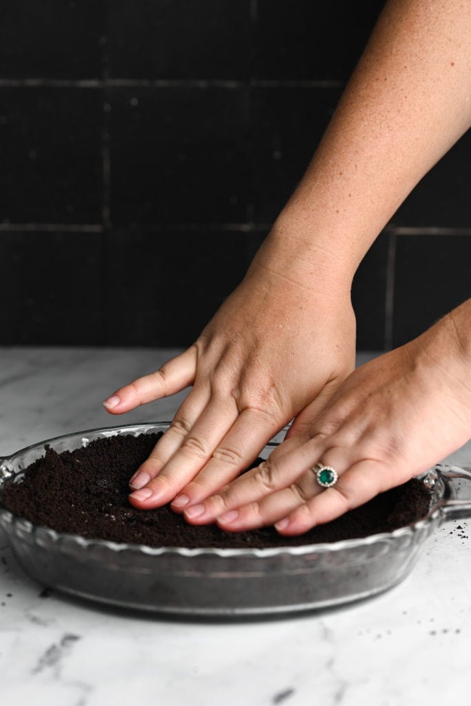 Using hands to push oreo and butter combo into a pie dish