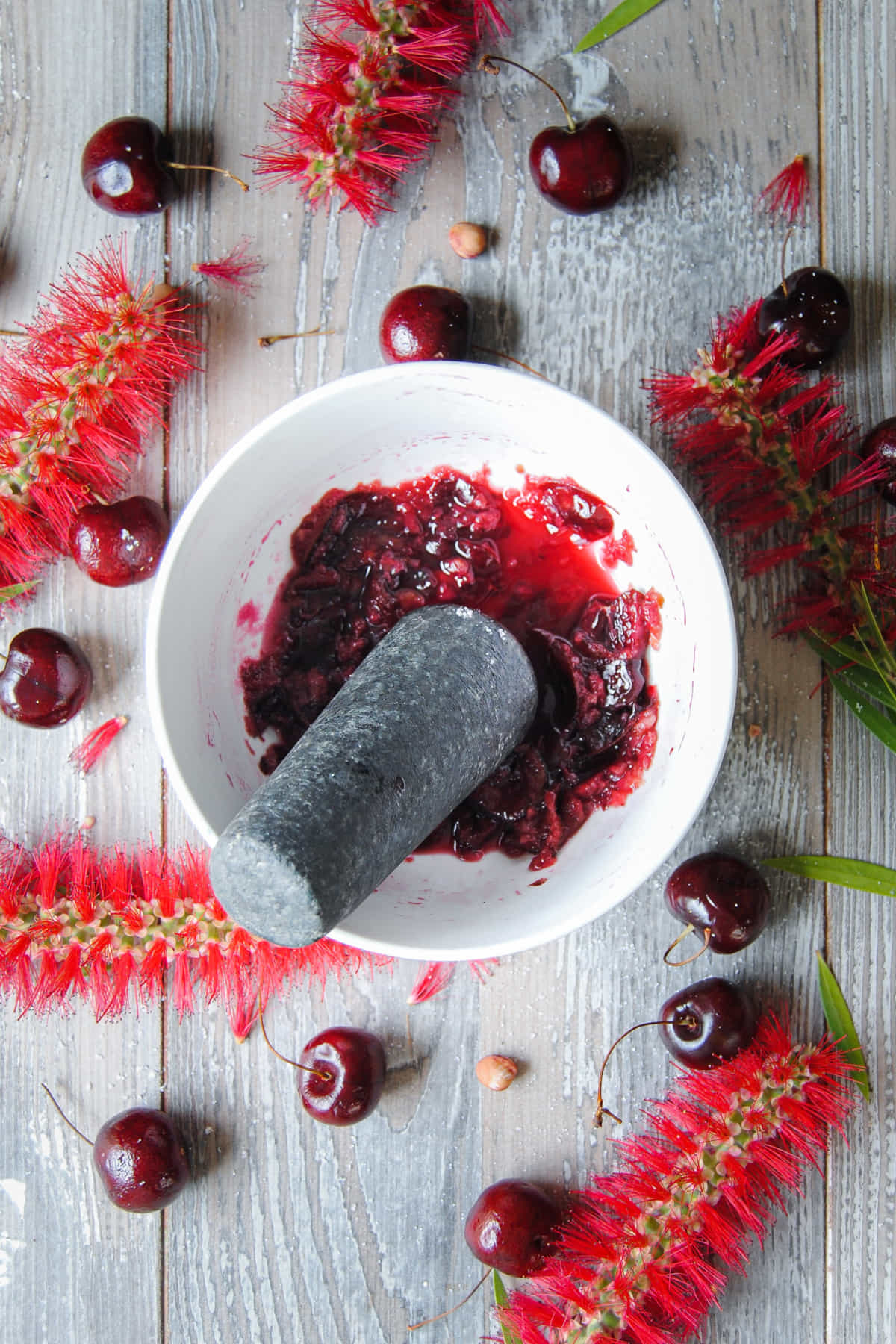 Muddling fresh cherries with sugar to extract the juice and sweeten.