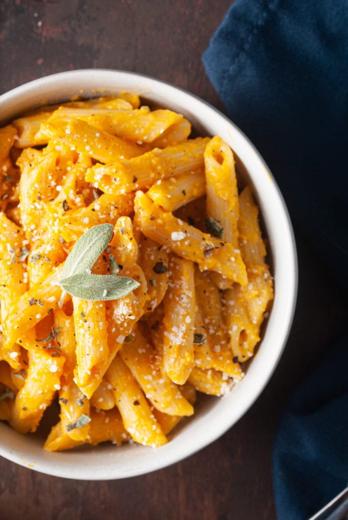 close up of pasta with pumpkin sauce garnished with parmesan, black pepper, and sage