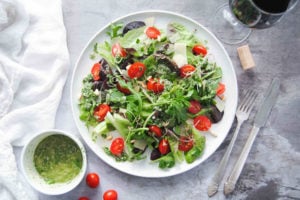 picture of green salad with tomatoes surrounded by vinaigrette and wine and utensils