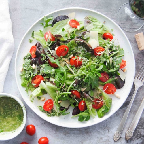picture of green salad with tomatoes surrounded by vinaigrette and wine and utensils