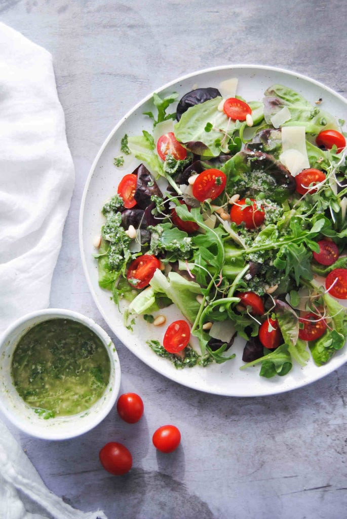 picture of salad with tomoatoes and little pot of green vinaigrette next to it