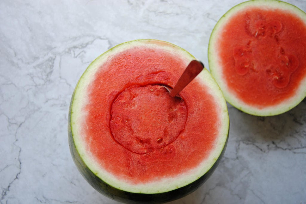 using a spoon to carve a hole in the center of a watermelon