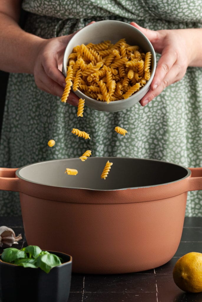 adding rotini pasta to a large pot of coiling water