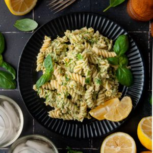 serving of tuna pesto pasta on a black plate surrounded by lemon and basil