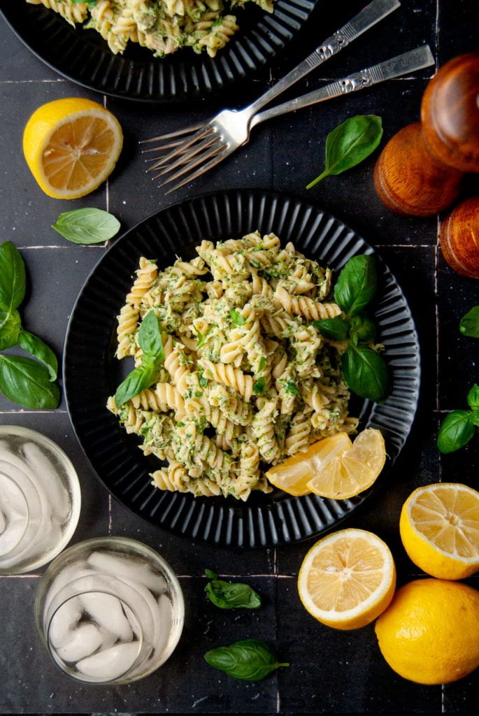serving of tuna pesto pasta on a black plate surrounded by lemon and basil