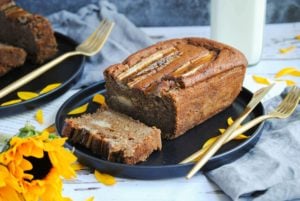 vegan banana bread on a plate with one slice cut and sunflowers
