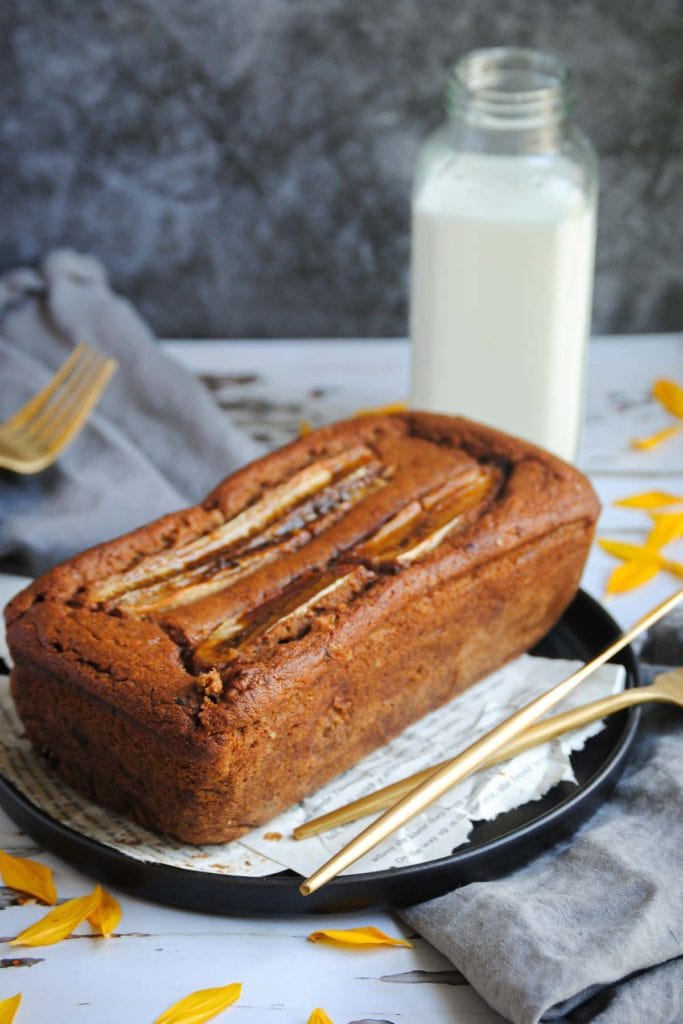 a whole banana bread with milk behind it and a fork and knife
