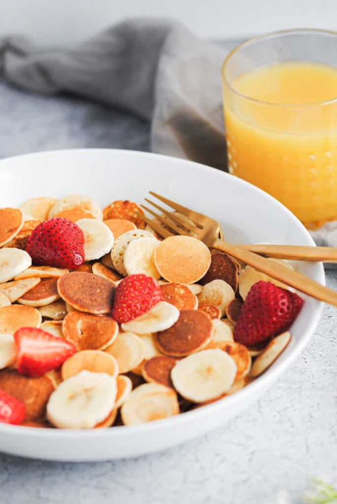 portrait of baby banana pancakes in a bowl with strawberries and gold forks