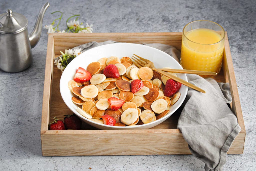 bowl of mini pancakes with strawberries on a breakfast tray with juice