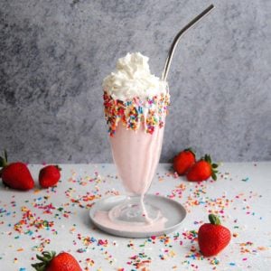 pink milkshake with whipped cream surrounded by sprinkles and strawberries