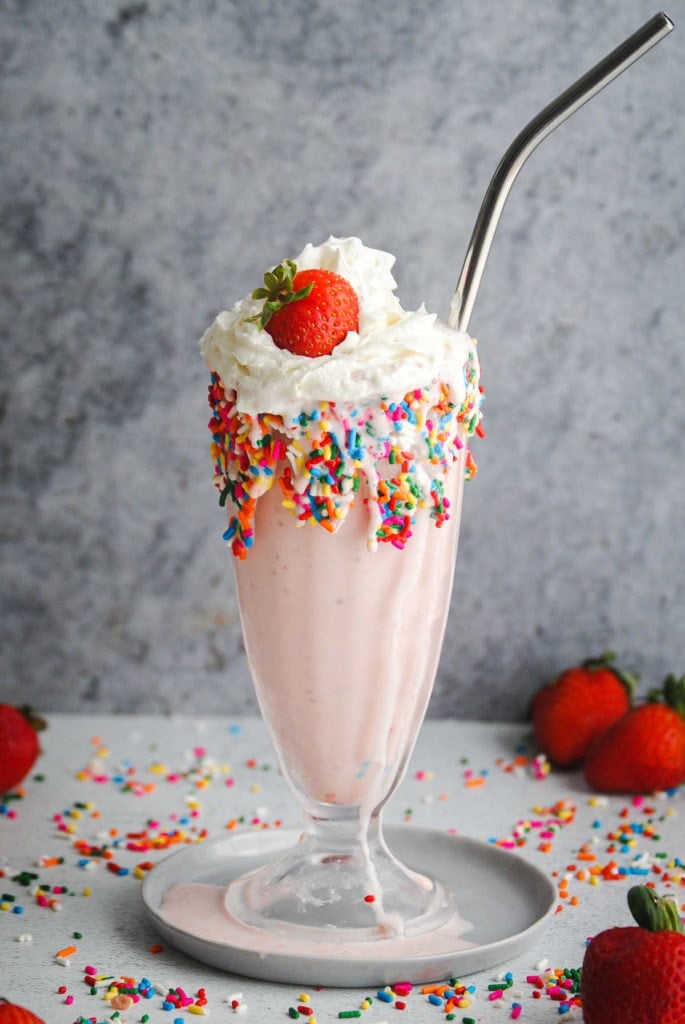 glass with pink shake and rainbow sprinkles garnished with a strawberry