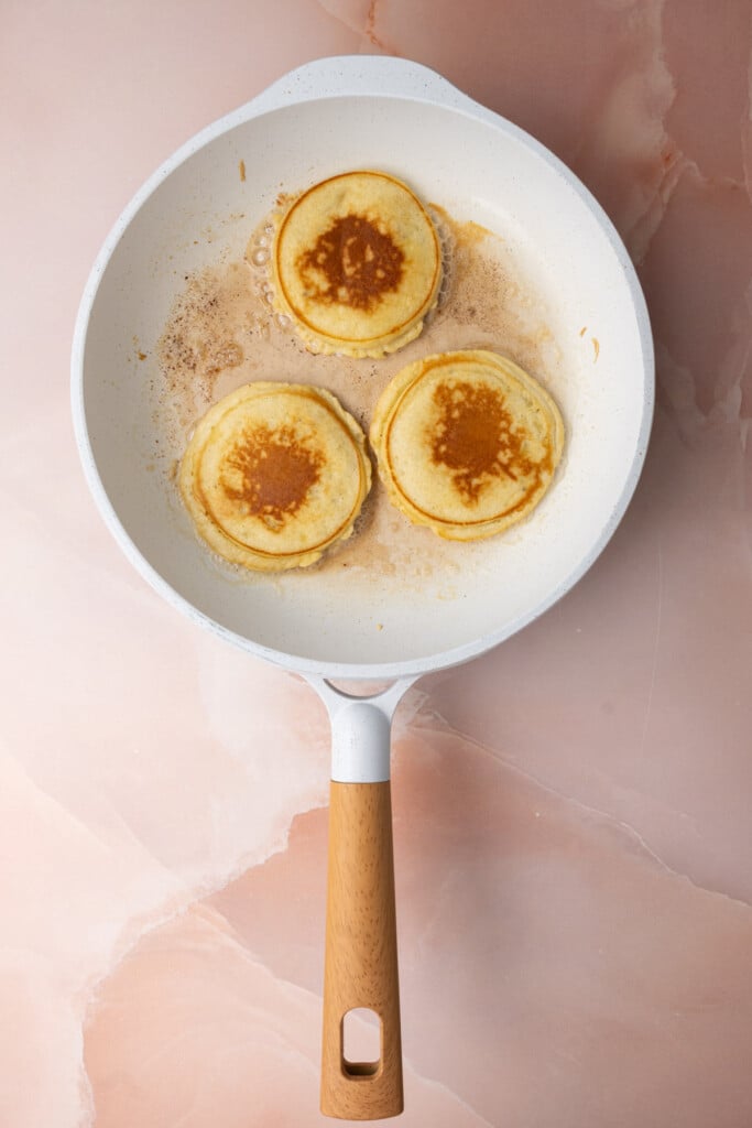 Golden brown banana pancakes still frying in butter in a pan. 
