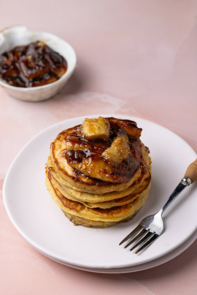 Tall stack of pancakes with bananas foster topping on a pink marble background. 