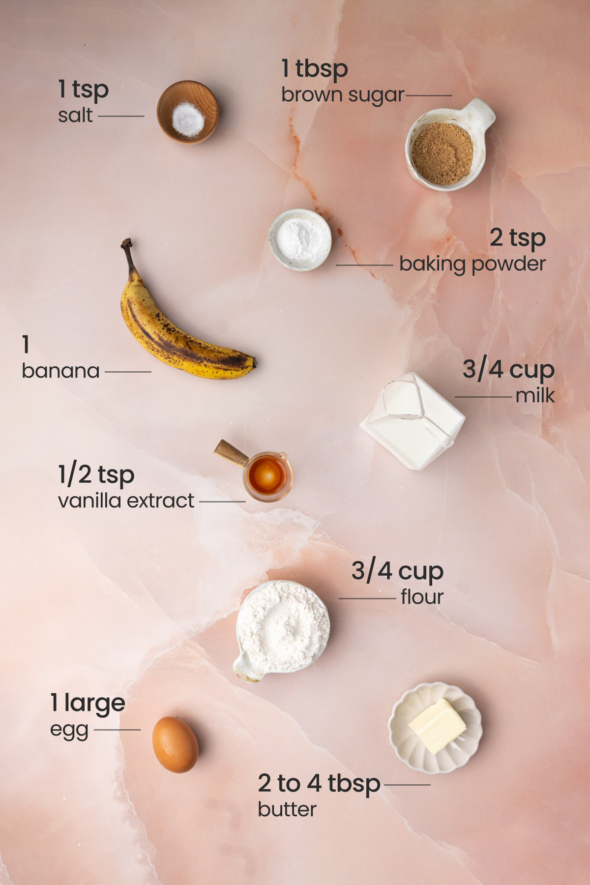 Overhead ingredients for Bananas Foster Pancakes - salt, brown sugar, baking powder, banana, milk, vanilla extract, flour, egg, and butter.