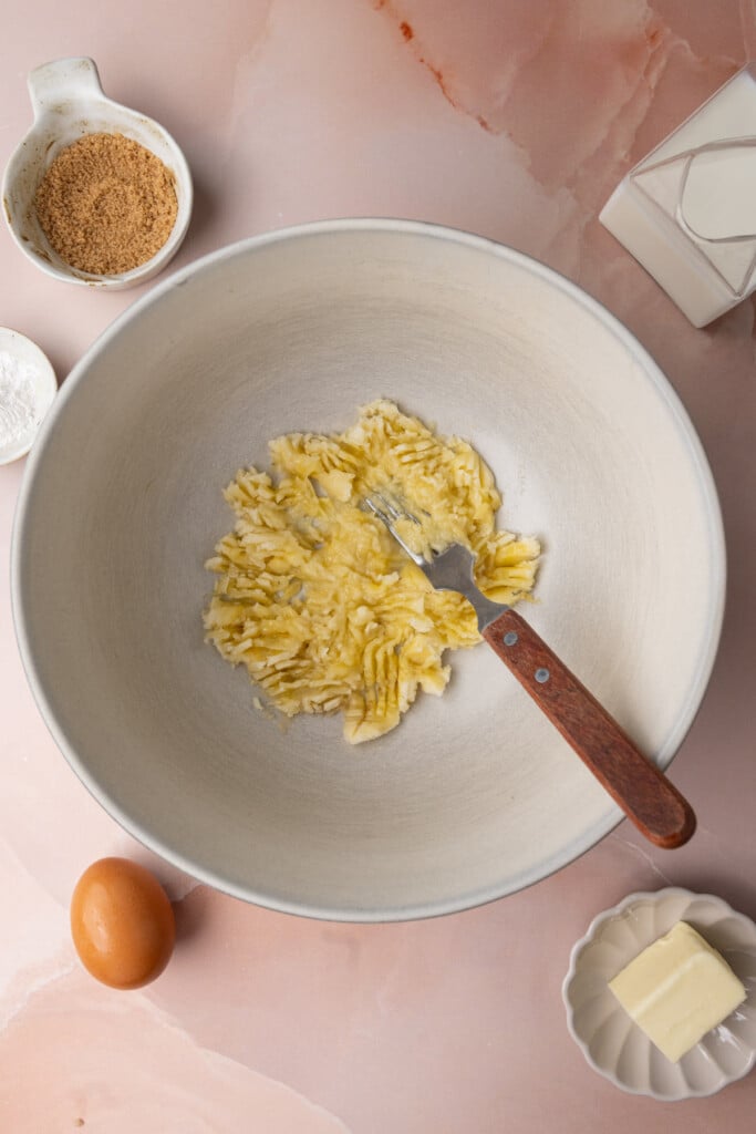 Banana mashed with a fork in a large mixing bowl. 