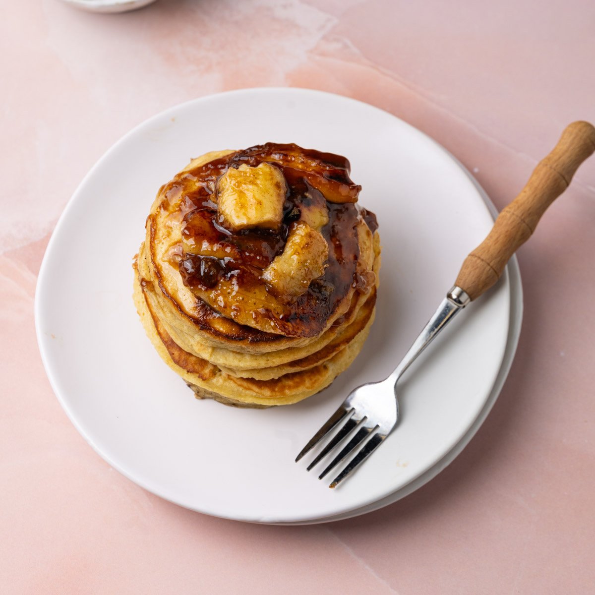 Tall stack of bananas foster pancakes with a fork on the plate.