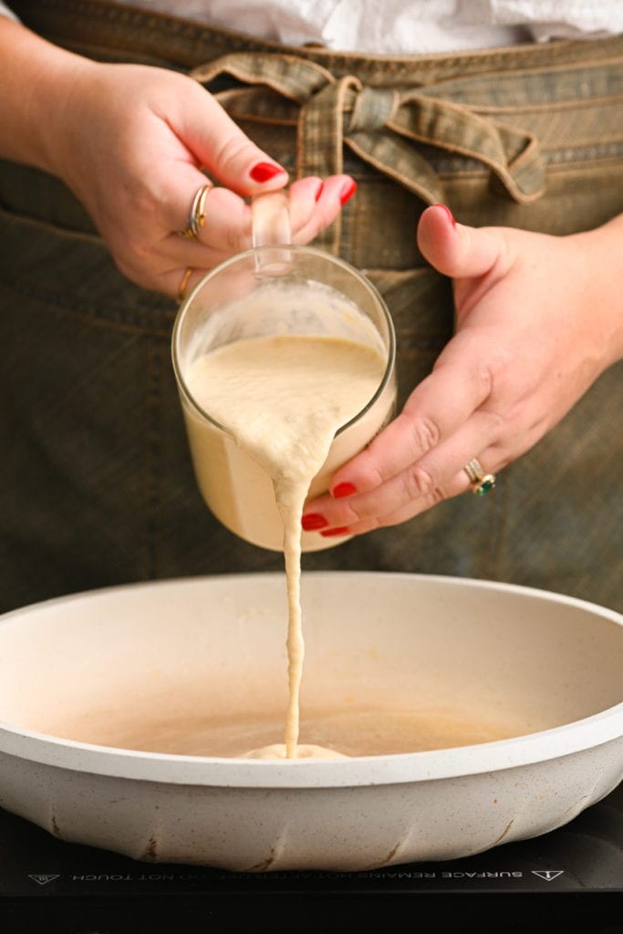 pouring pancake batter from measuring cup into hot pan with butter