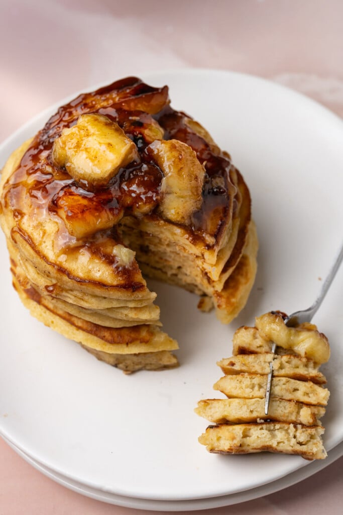 Stack of banana pancakes topped with bananas foster with a big bite on a fork.