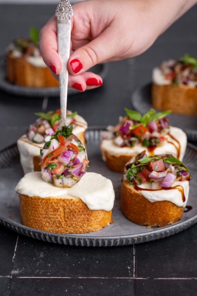 adding spoonful of bruschetta onto french baguette with melted mozzarella cheese