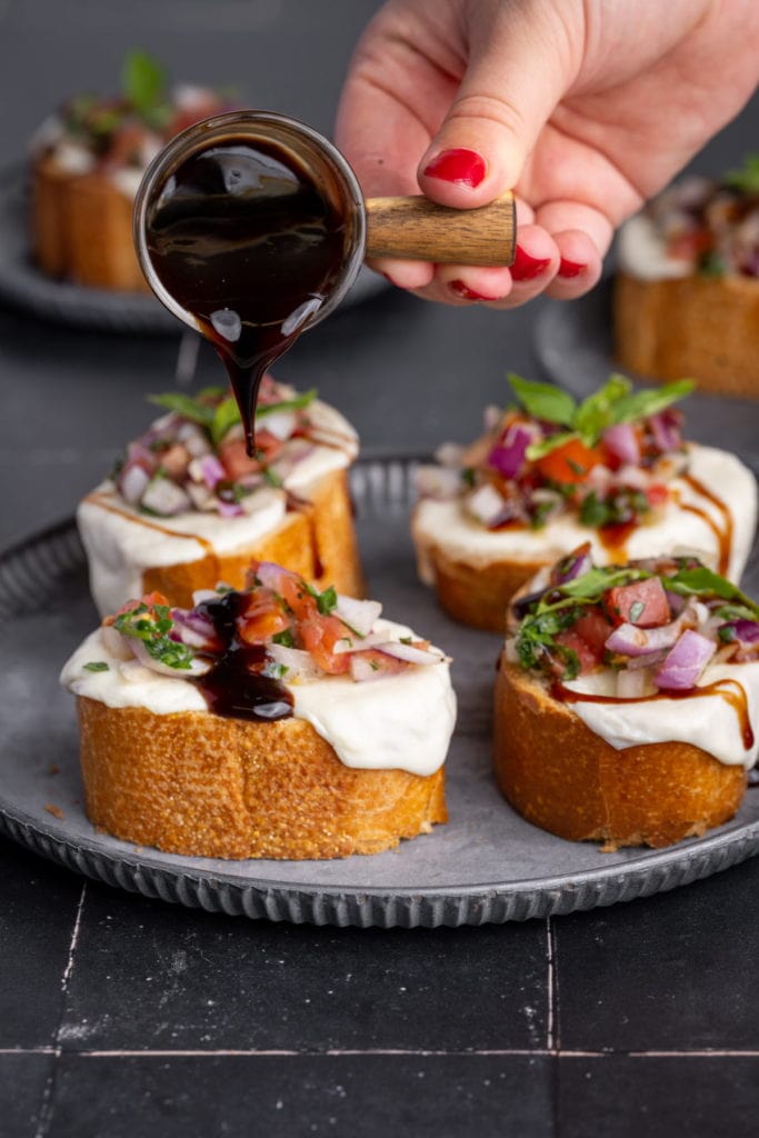 pouring balsamic glaze onto caprese bruschetta