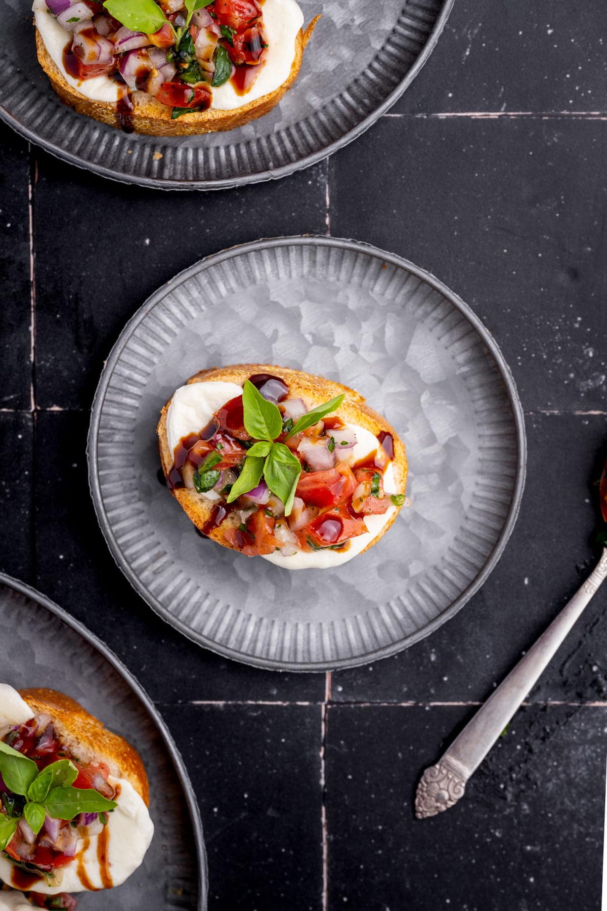 Caprese bruschetta crostini on a plate with fresh basil and balsamic glaze drizzled on top.