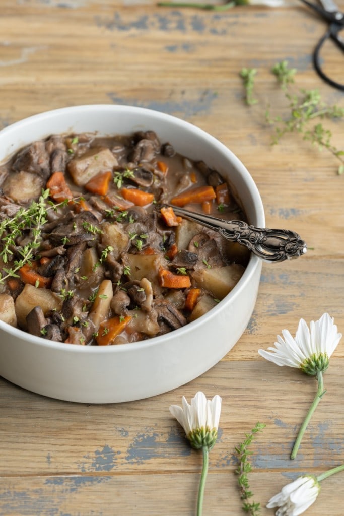 serving bowl with mushroom stew on wood table surrounded by flowers
