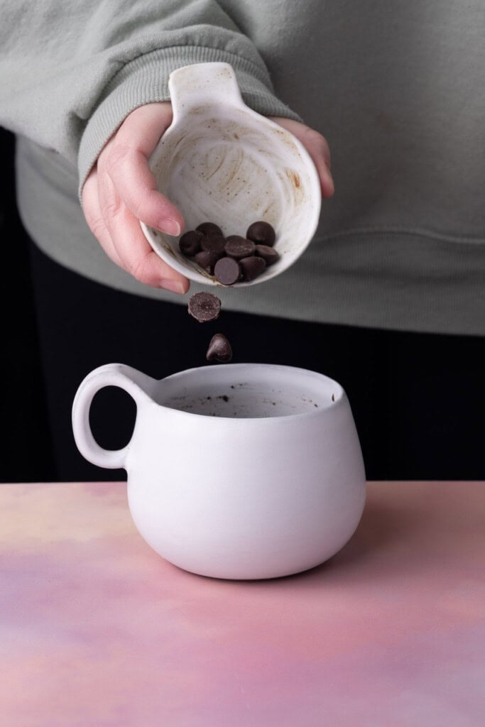Adding chocolate chips to a mug to make a microwave cake.