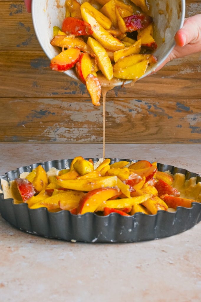 pouring peach mango pie filling into crust in a pie dish