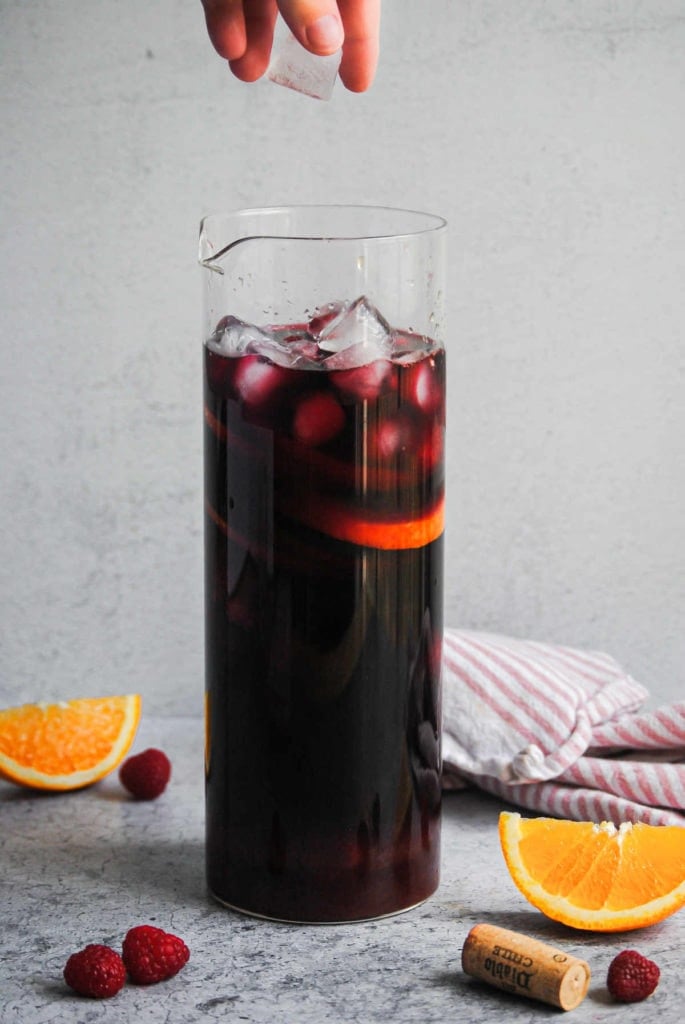 adding ice to a pitcher of raspberry sangria