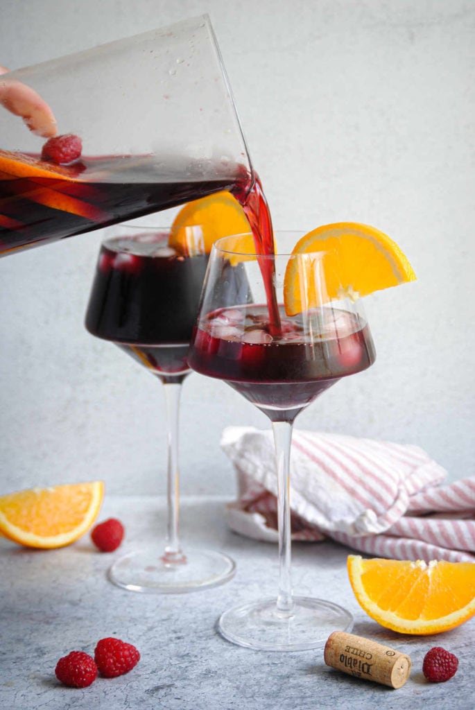 pouring raspberry sangria from pitcher into individual wine glasses