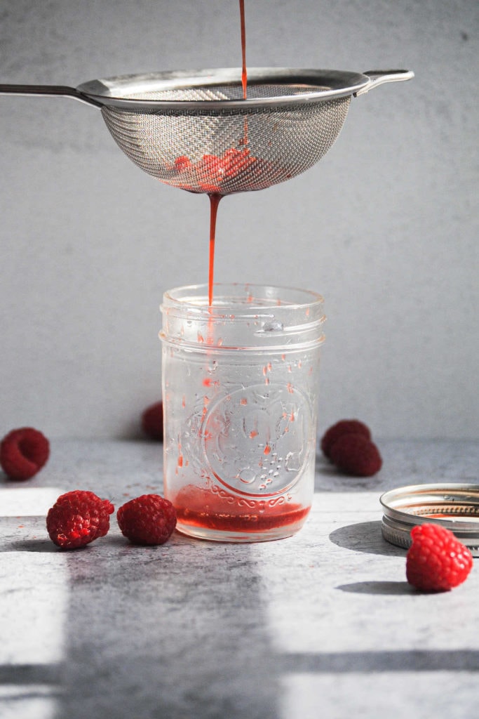straining raspberry simple syrup through a sieve into a small mason jar