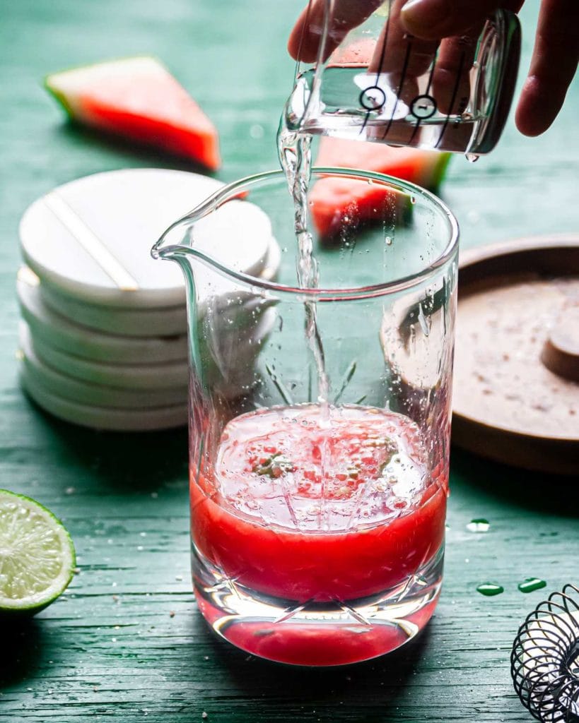 pouring tequila into mixing glass with watermelon and basil