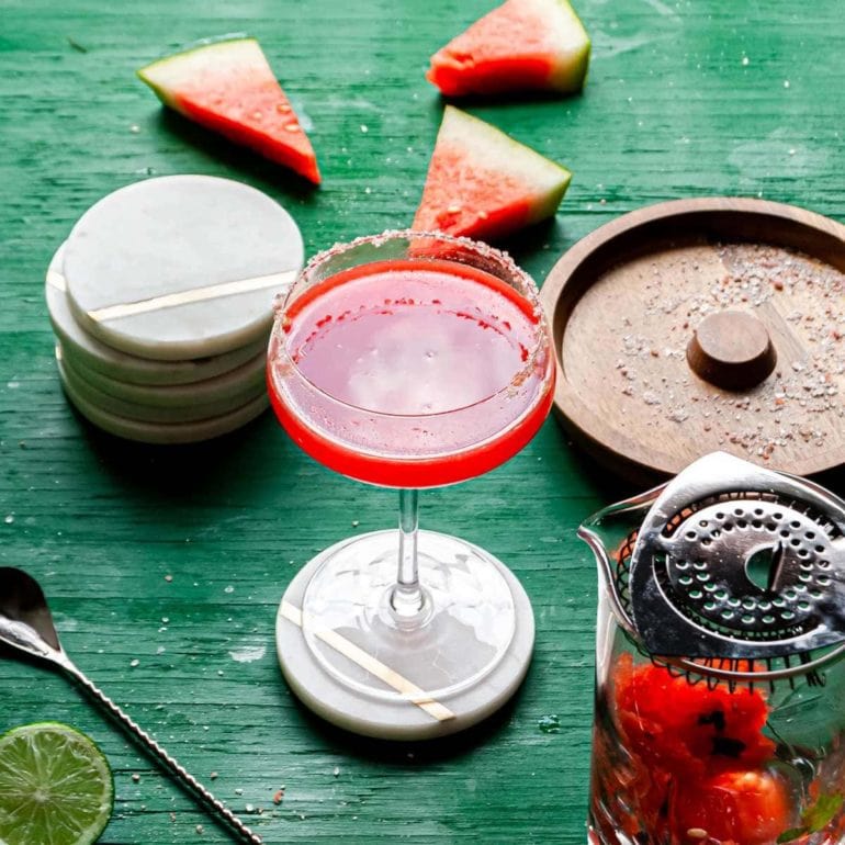 pink margarita in coupe glass with salted rim surrounded by watermelon