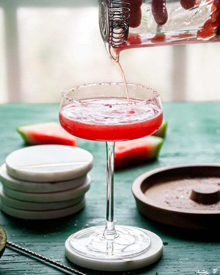 Pouring watermelon margarita into cocktail glass with salted rim