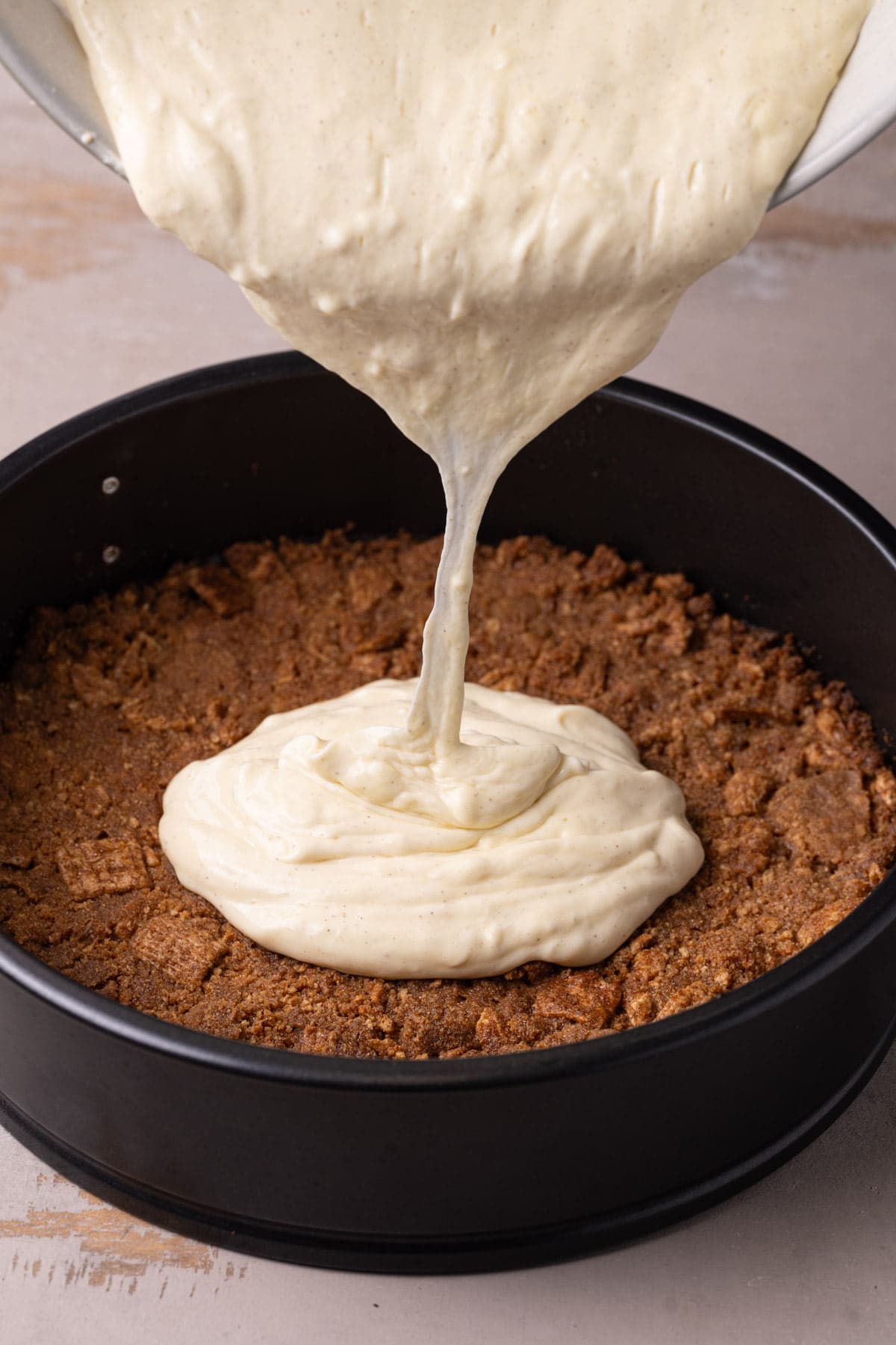 Pouring cheesecake filling into cinnamon toast crunch crust. 