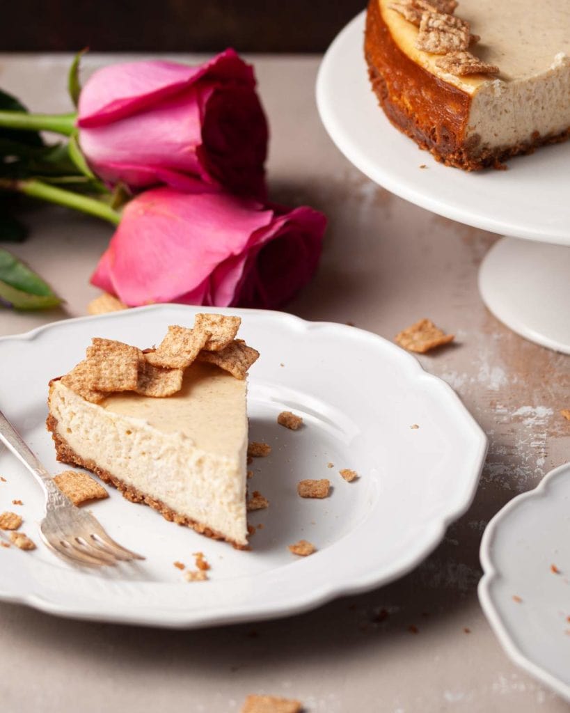 Slice of Cheesecake in front of roses and a cake stand