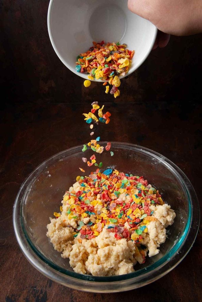 pouring fruity pebbles into cookie dough