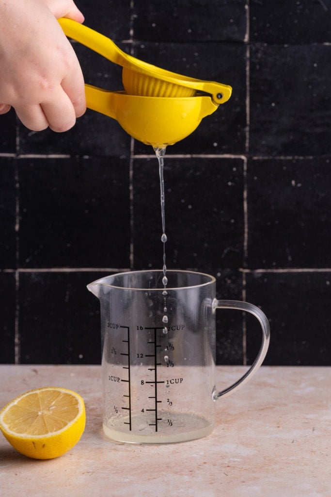 Using yellow juicer to squeeze lemon juice into a measuring cup