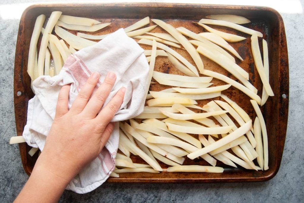 using a clean kitchen towel to dry off uncooked french fries after soaking them in water