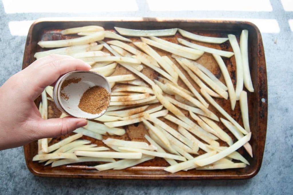 pouring old bay seasoning over french fried before baking